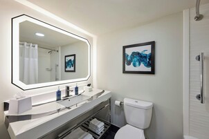 Un baño moderno con un espejo grande, un inodoro, una ducha y un lavabo con toallero.