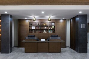 A reception desk with a wooden finish, flanked by dark wall panels and a tiled floor. - Four Points by Sheraton Englewood (Englewood)