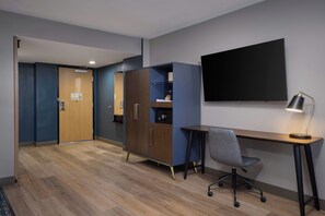 Habitación de hotel con un escritorio de madera, una silla, un televisor montado en la pared y un armario.
