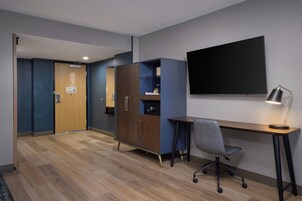 Habitación de hotel con un escritorio de madera, una silla, un televisor montado en la pared y un armario.