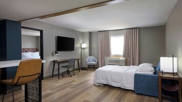 Habitación de hotel con cama, escritorio, silla, televisor y ventana con cortinas.