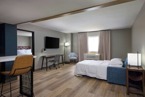 Habitación de hotel con cama, escritorio, silla, televisor y ventana con cortinas.