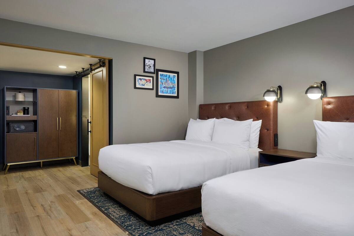 A hotel room with two beds, a wardrobe, a desk, and a nightstand.