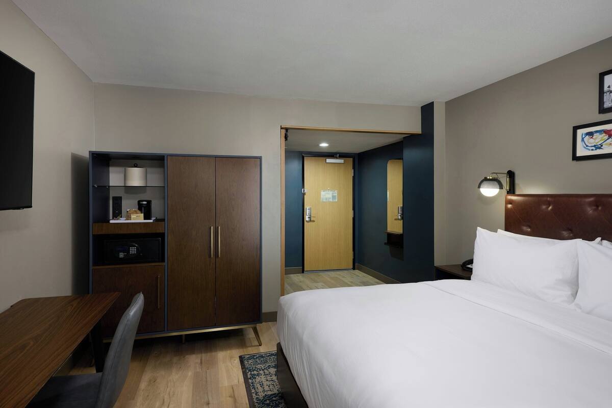 A hotel room with a bed, a desk, a wardrobe, a mirror, and a nightstand.