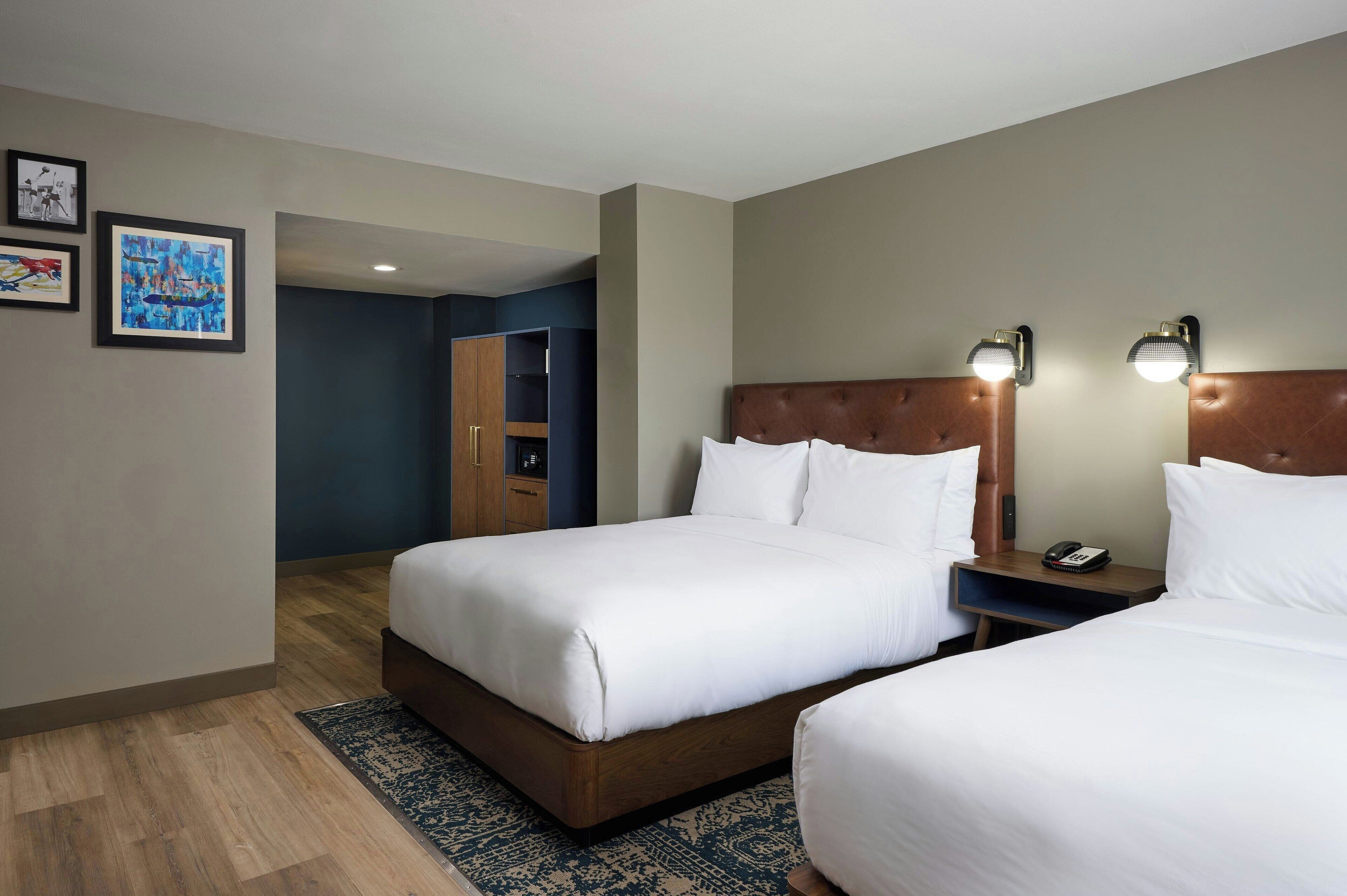 Une chambre d’hôtel avec deux lits, une tête de lit en bois, une table de chevet avec un téléphone et un mur bleu orné d’œuvres d’art.