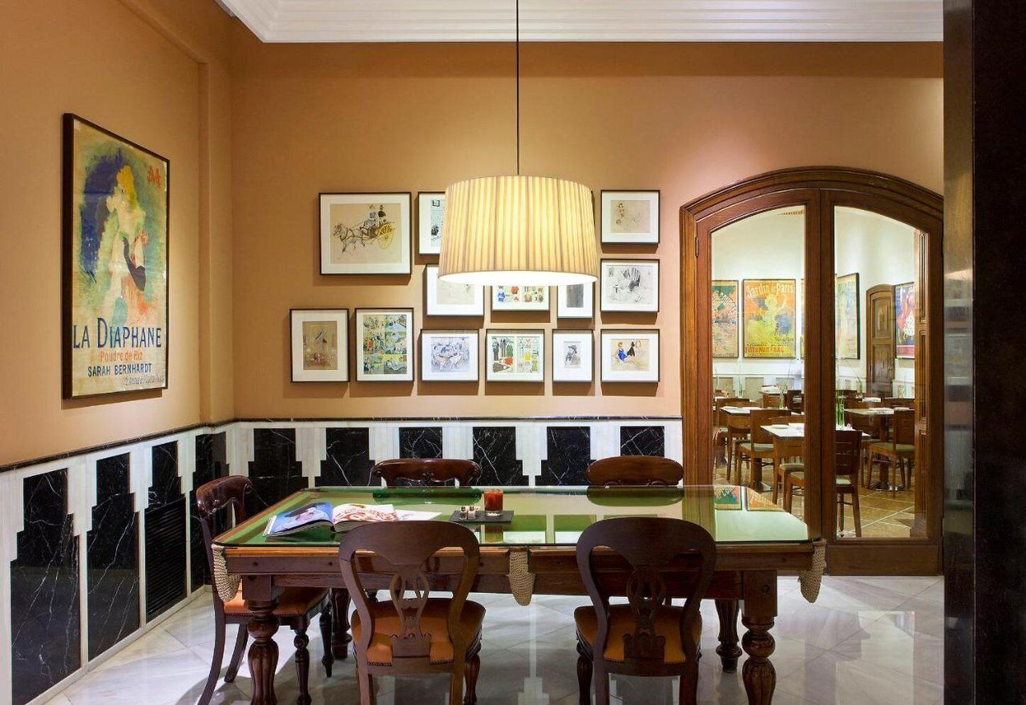 A dining area with a billiards table, wooden chairs, and framed artwork on the walls.