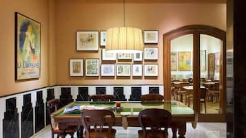 A dining area with a billiards table, wooden chairs, and framed artwork on the walls.