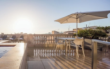 A rooftop pool area with a sunken seating area, a table with chairs, and an umbrella.