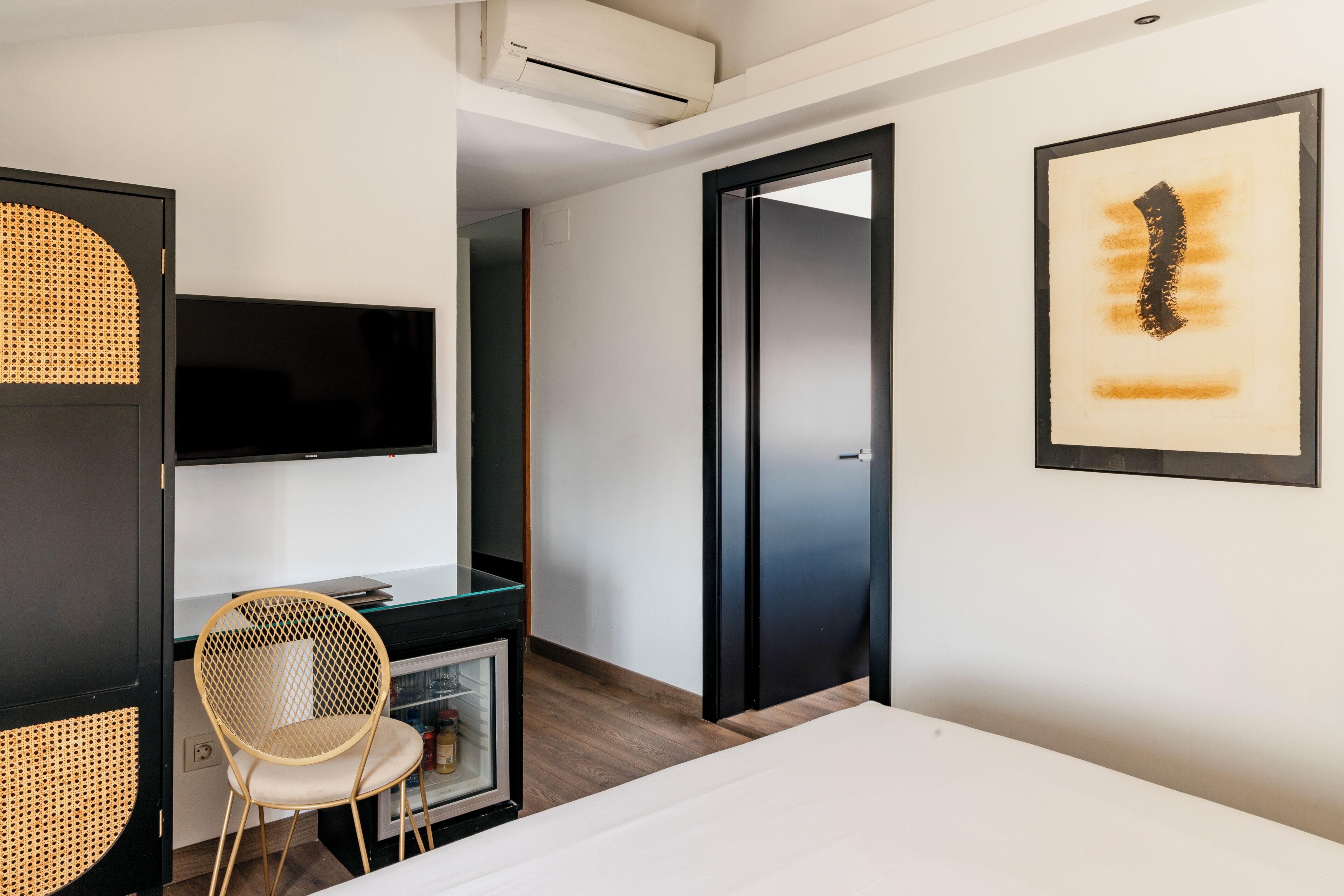 Moderni hotellihuone, jossa on sänky, työpöytä tuolilla, televisio ja taideteoksia seinällä.