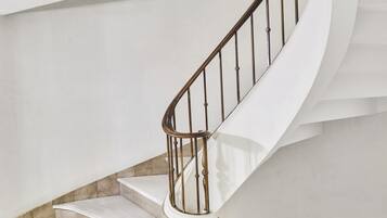 Una escalera curva con barandilla de metal, escalones de mármol y pared blanca.