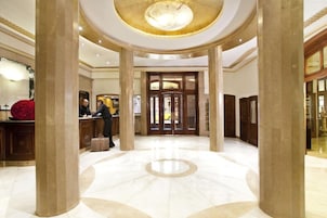 A grand lobby with marble flooring, large columns, and a reception desk.