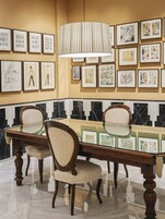 A dining area with a marble-tiled floor, a glass-top table, two upholstered chairs, and framed artwork on the walls.