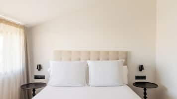 Una habitación de hotel con una cama, dos mesitas de noche, un cabecero y una ventana con cortinas.