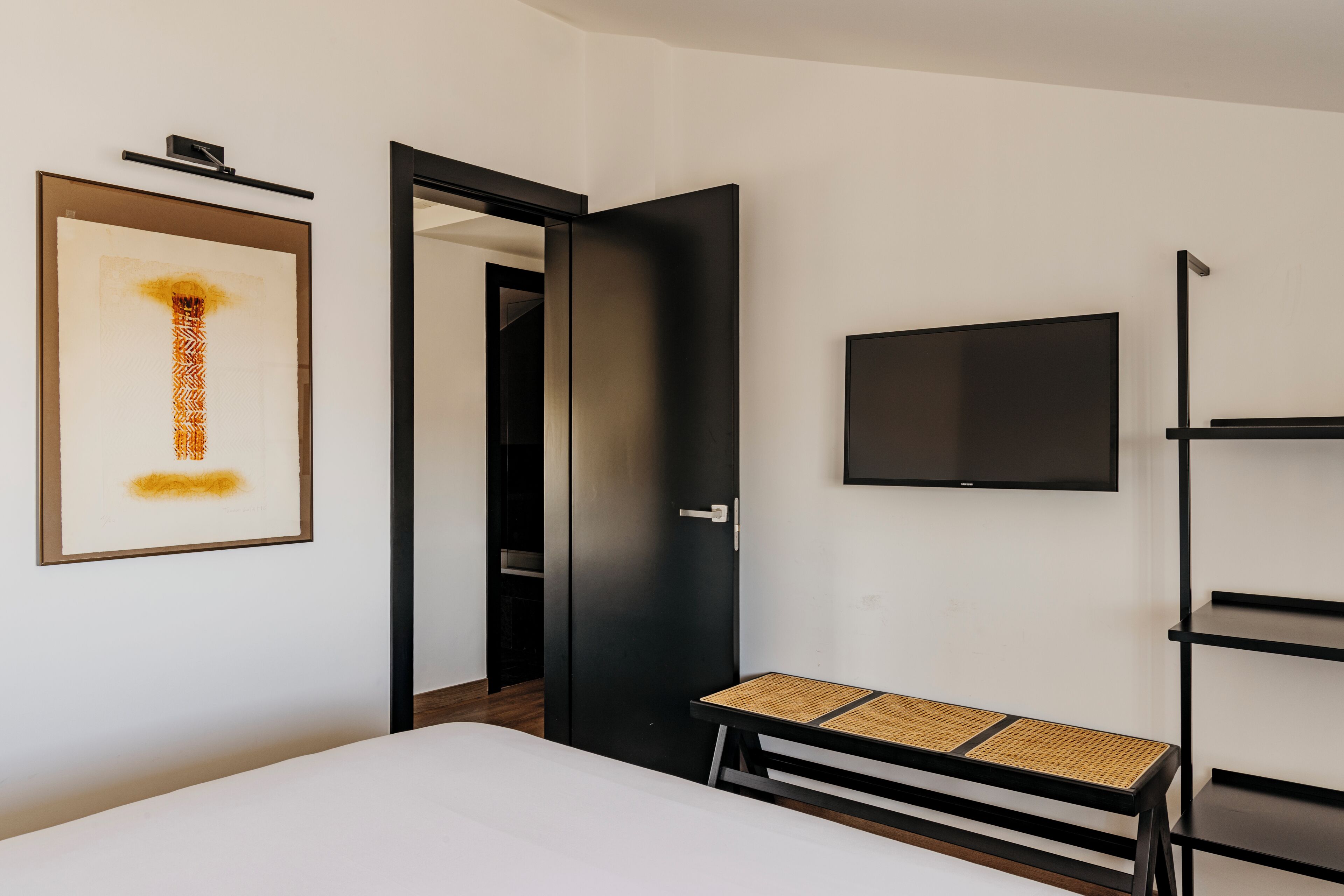 Una habitación de hotel moderna con una cama, un televisor, una obra de arte enmarcada y una puerta que da a un pasillo.