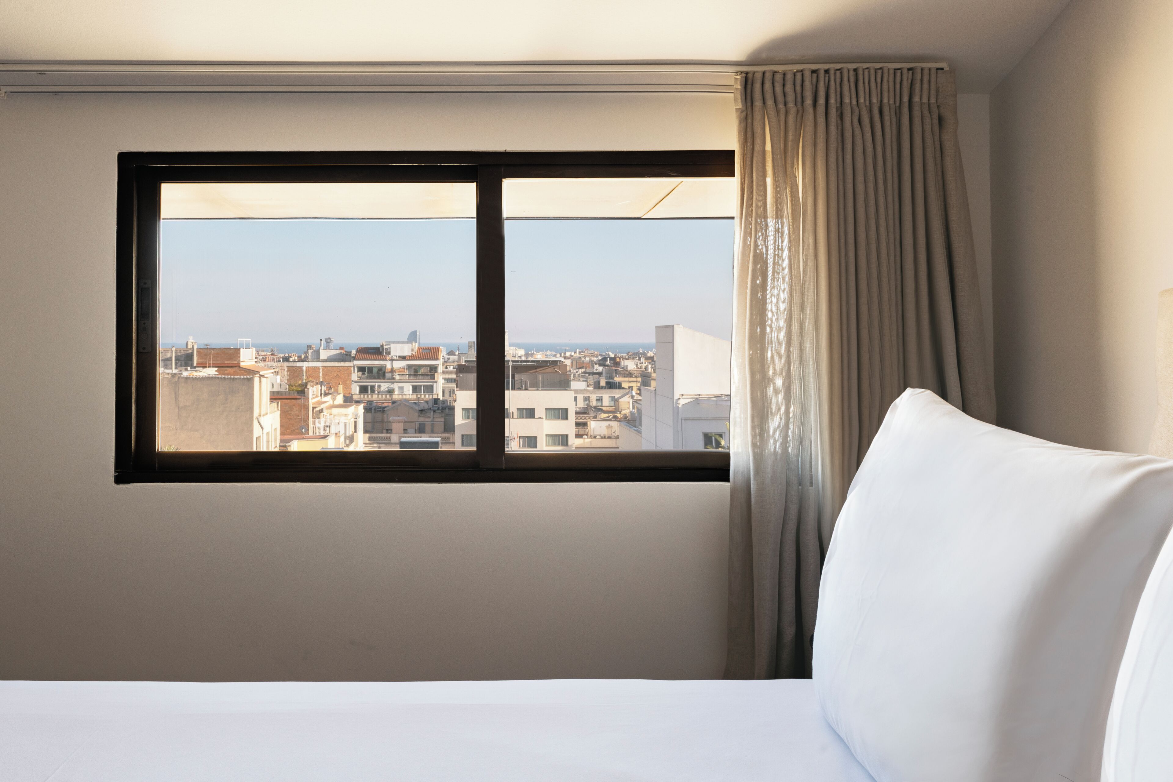 A hotel room with a large window, a bed, and a view of the cityscape.