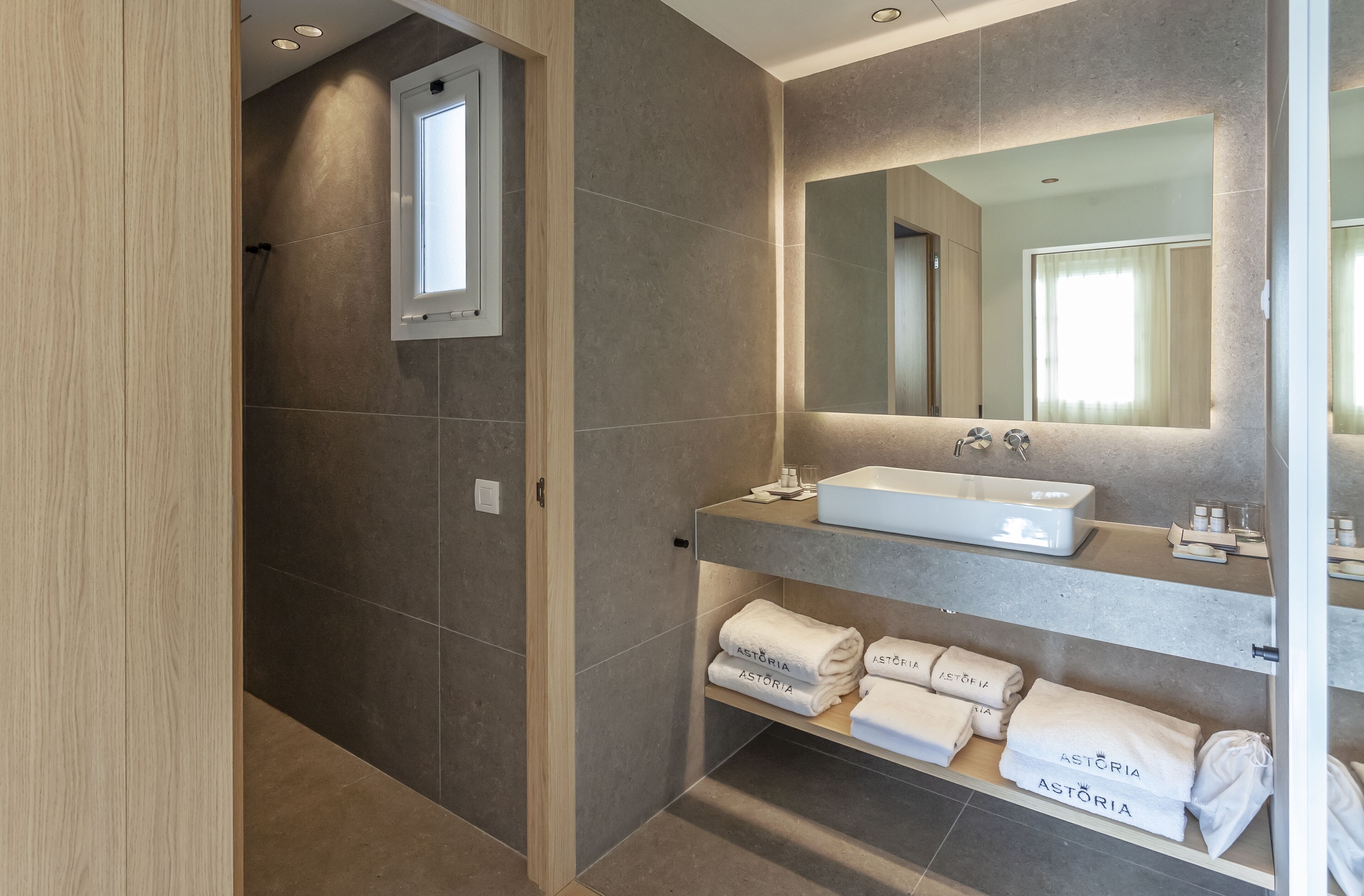 A modern bathroom with a large mirror, a built-in sink, and shelves with folded towels.
