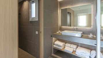 A modern bathroom with a large mirror, a built-in sink, and shelves with folded towels.