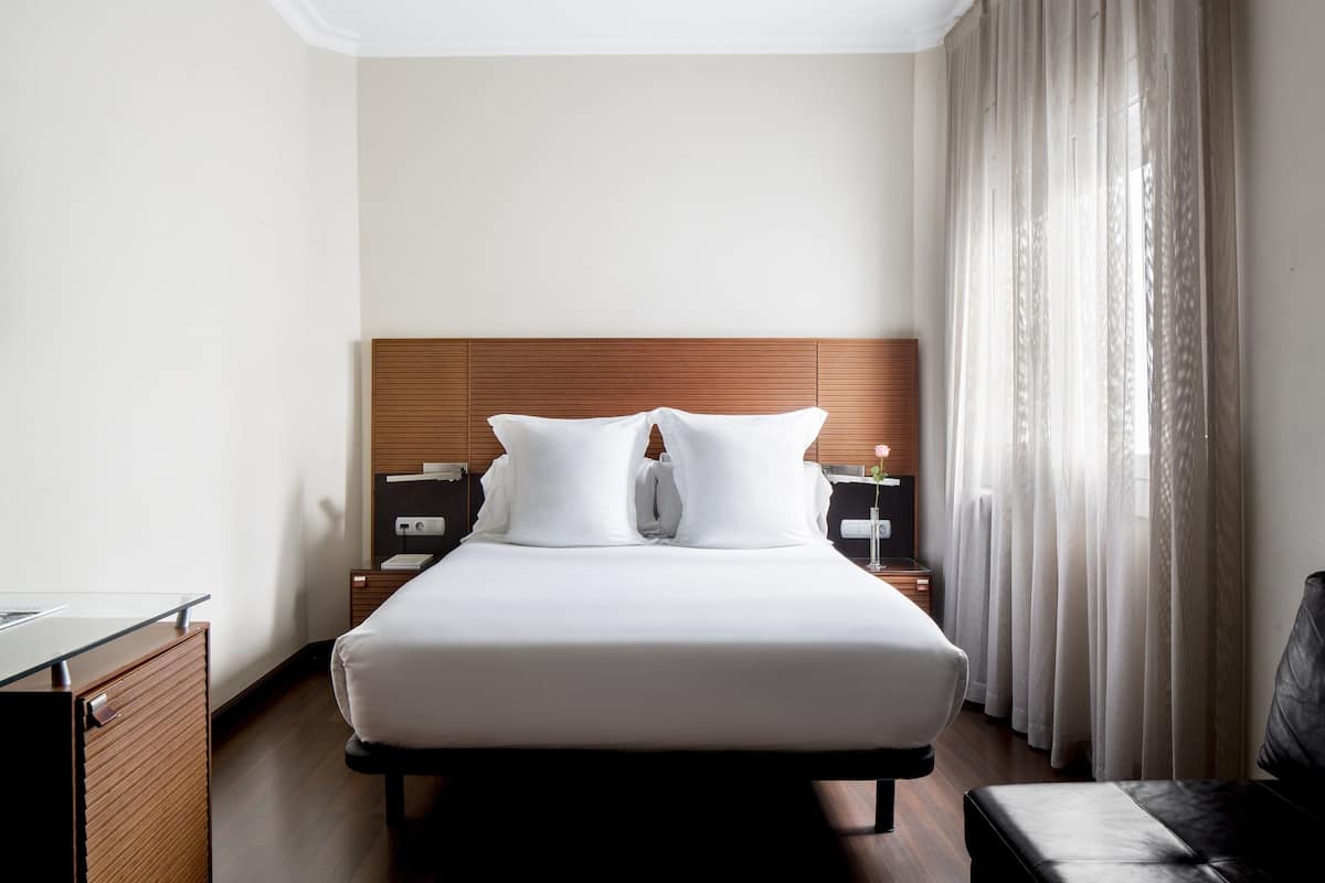 Een hotelkamer met een groot bed, een houten hoofdeinde, twee nachtkastjes, een bureau en een stoel.