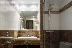 A bathroom with a marble sink, a glass shower enclosure, and a mirror reflecting a hallway.