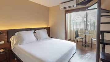 Una camera d'albergo con un letto, una scrivania, una sedia, un tavolino e una finestra vista palme.