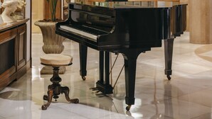 Un piano de cola en un vestíbulo amplio y elegantemente decorado, con suelo de mármol y elementos decorativos de estilo clásico.