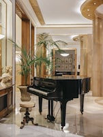 Um piano de cauda imponente num hall amplo, ricamente decorado com piso de mármore e elementos decorativos clássicos.