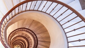 Una escalera de caracol con barandal de madera y escalones blancos.