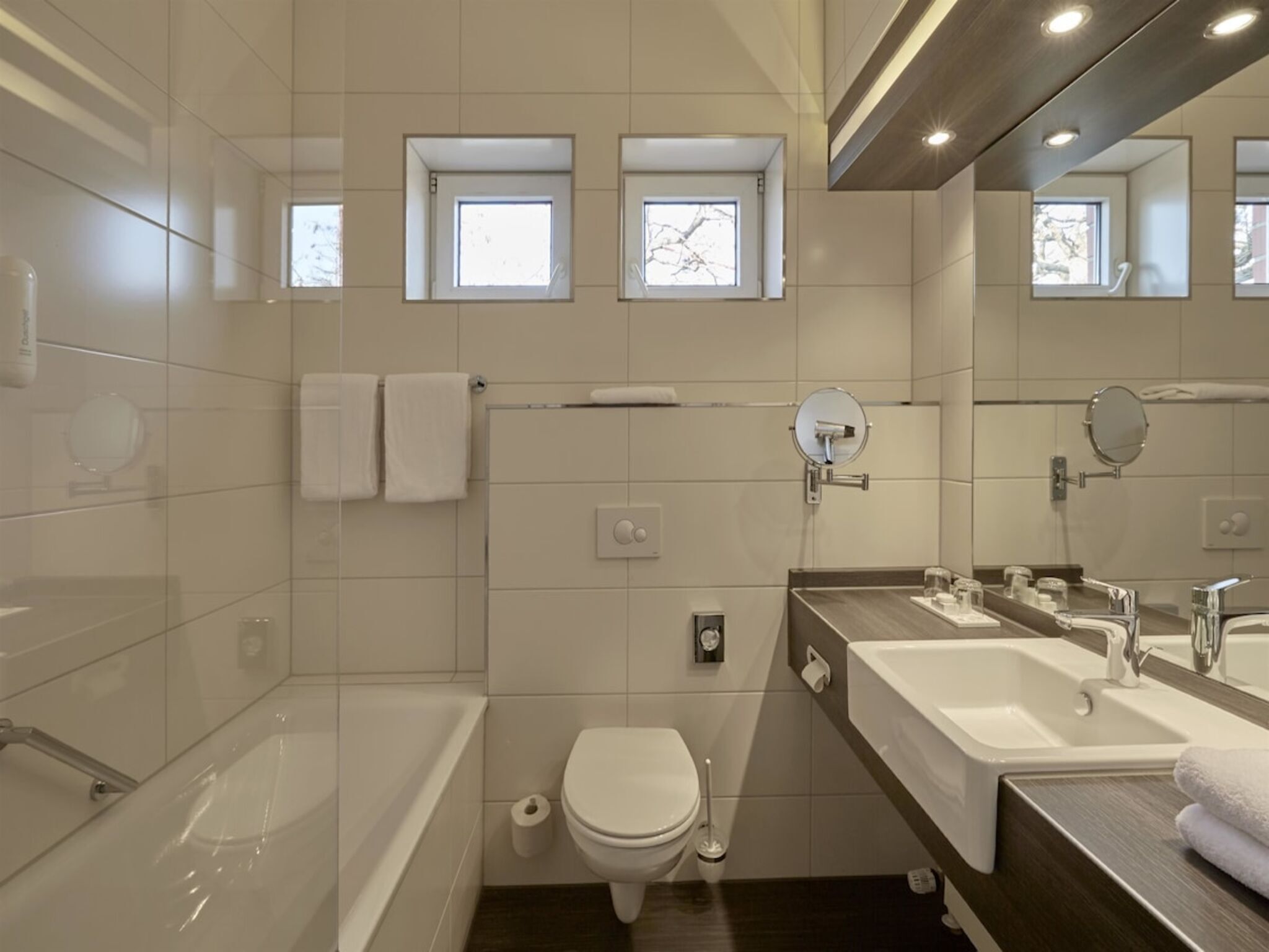 Un baño moderno con bañera, inodoro y dos lavamanos con espejos.