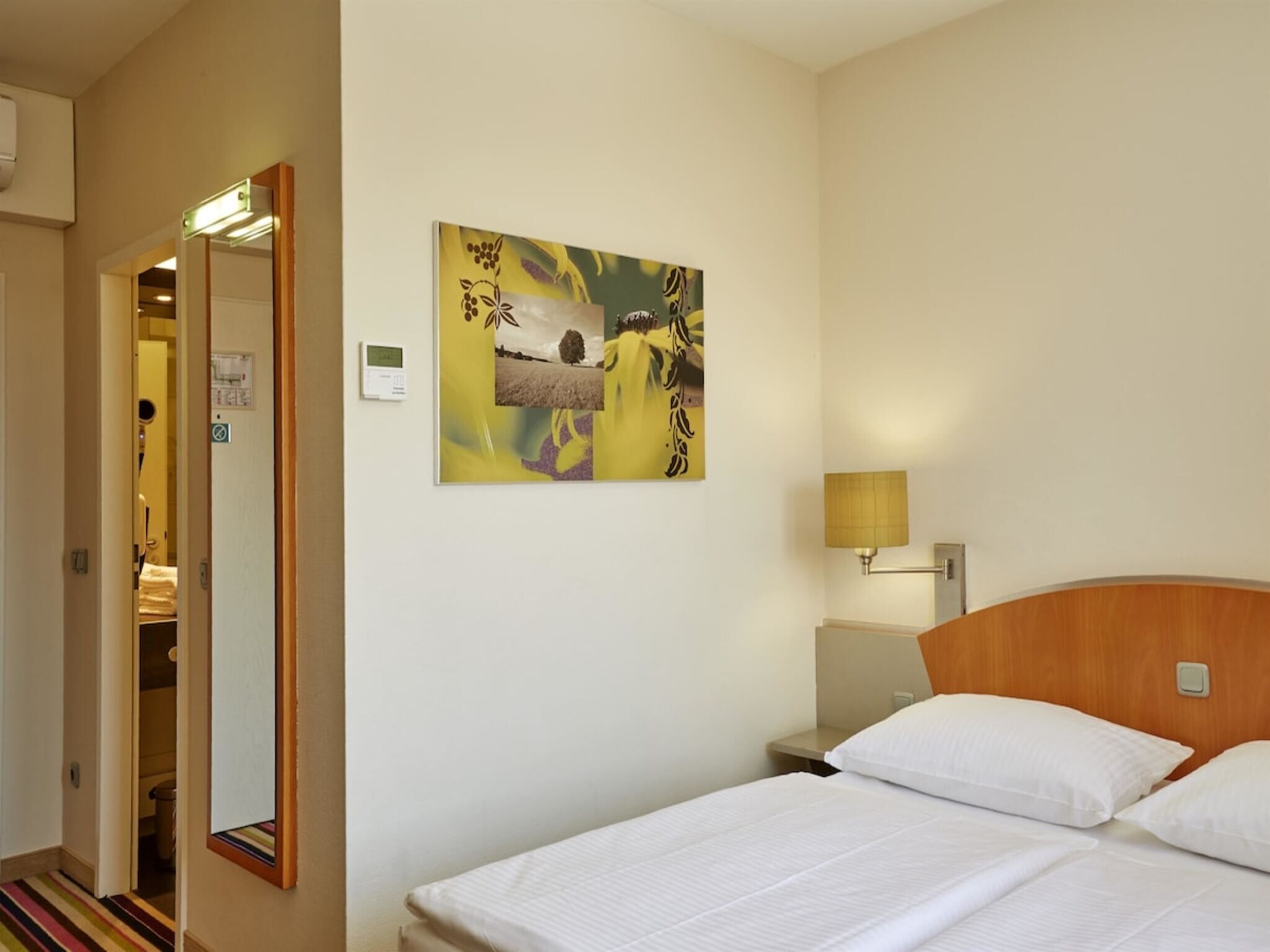 A hotel room with a bed, a nightstand, a lamp, and a wall-mounted artwork.