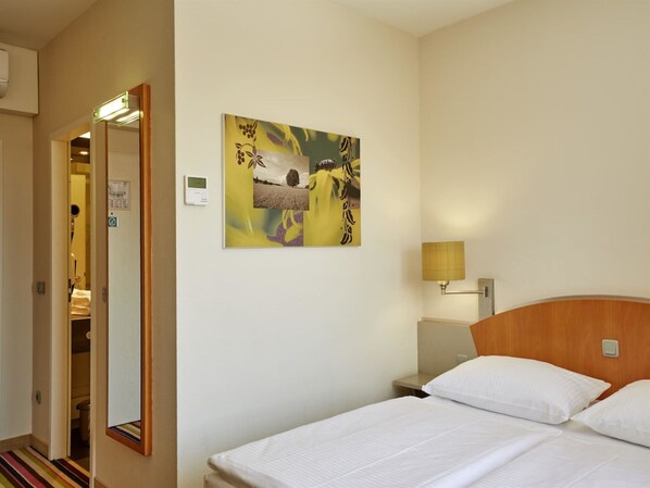 Una habitación de hotel con una cama, una mesita de noche, una lámpara y una obra de arte colgada en la pared.