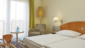 Una habitación de hotel con una cama, una silla, una mesita con botellas y una lámpara.