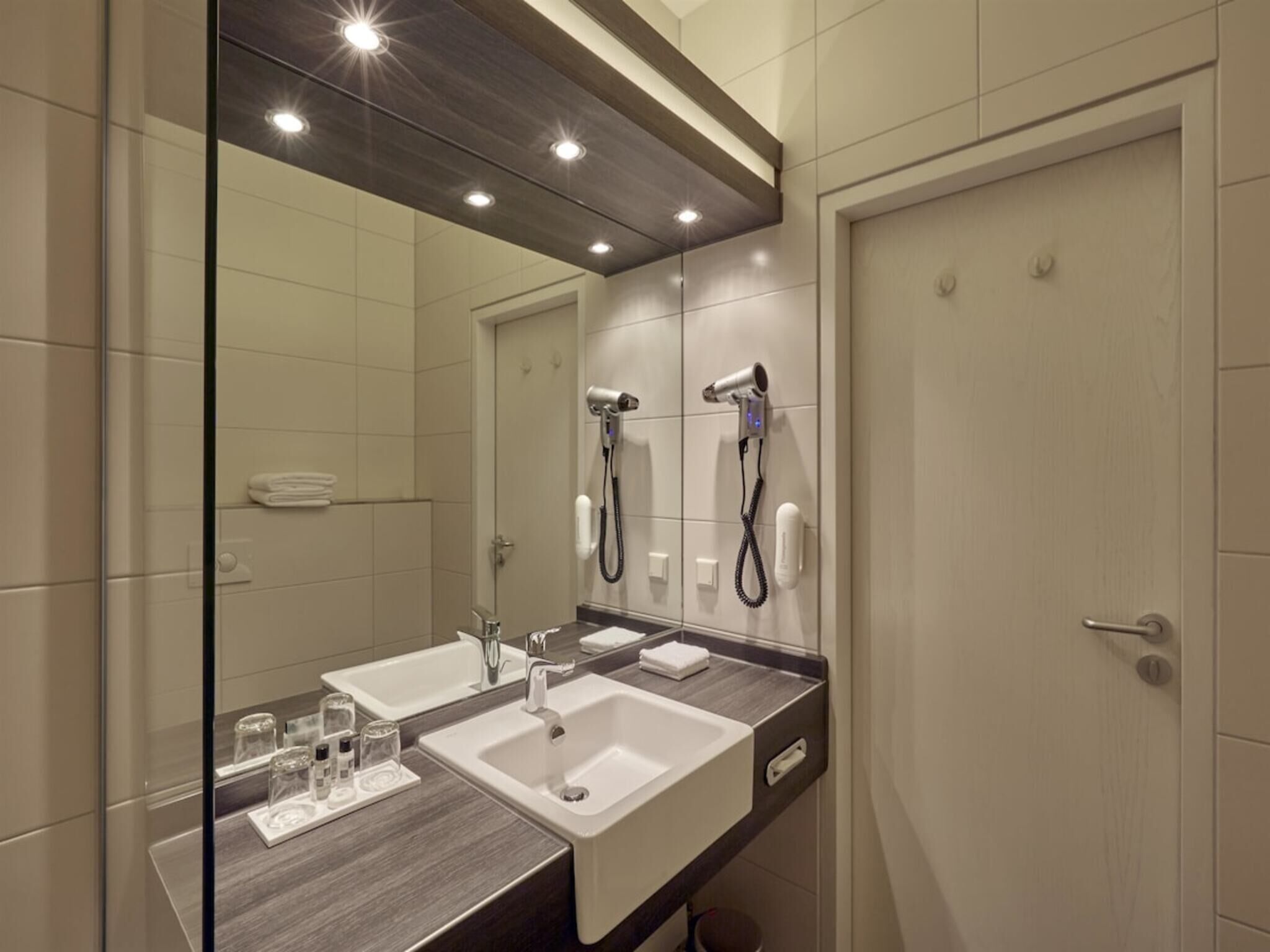 A modern bathroom with two sinks, a large mirror, and built-in hair dryers.