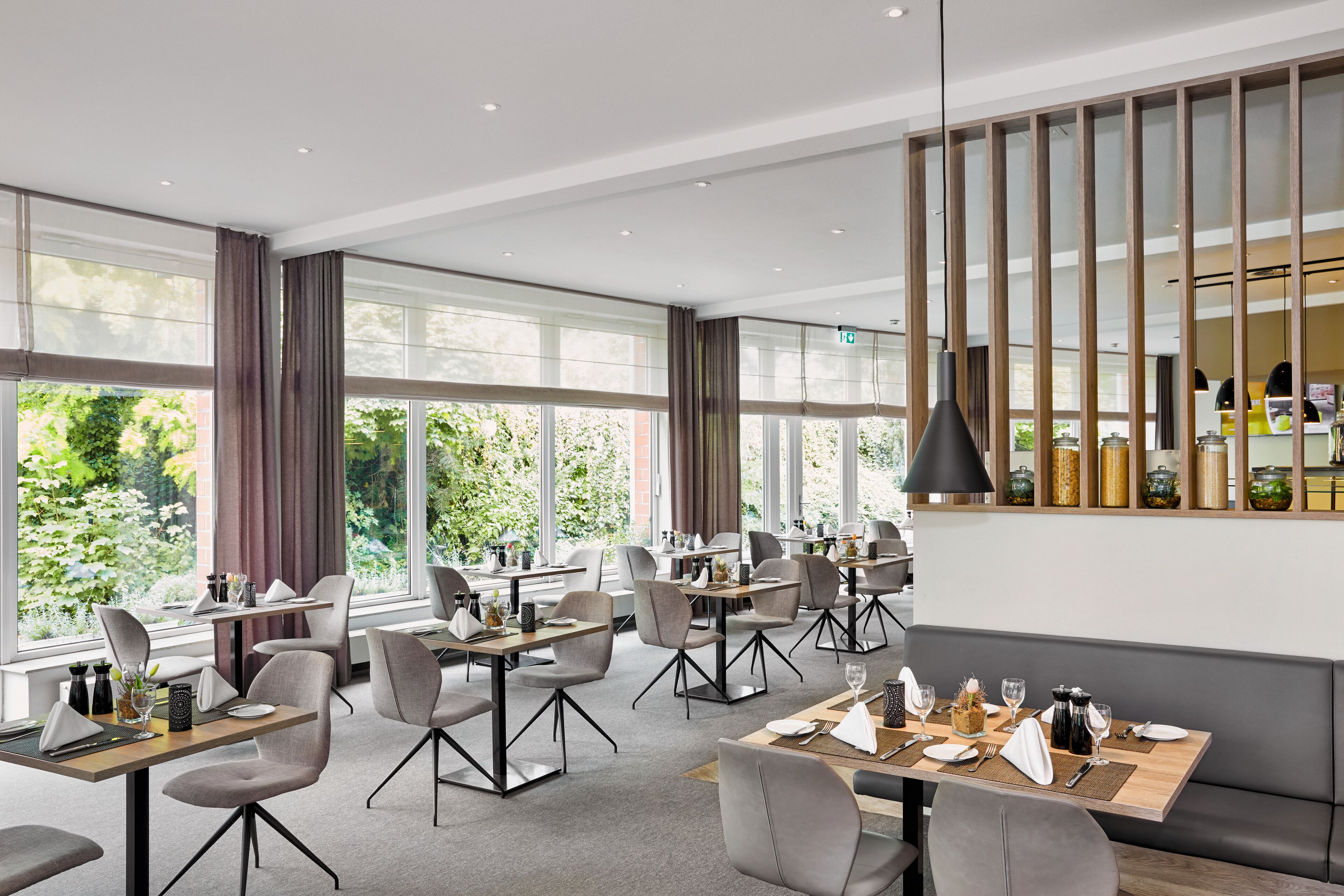 Een moderne eetruimte met tafels en stoelen, grote ramen en een decoratieve wand.