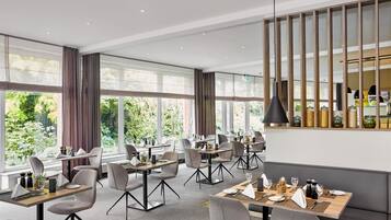 Een moderne eetruimte met tafels en stoelen, grote ramen en een decoratieve wand.
