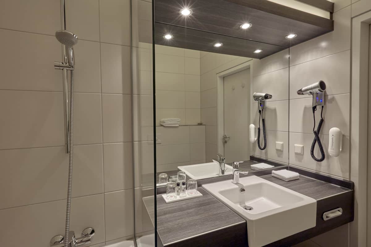 A modern bathroom with a glass shower enclosure, a double sink vanity, and a hairdryer mounted on the wall.