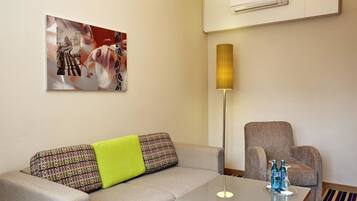 A modern hotel room with a sofa, armchair, and a table with a lamp.