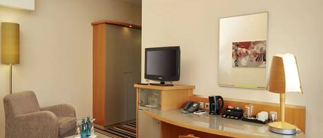 A hotel room with a sofa, a small table, a television, a desk with a telephone and coffee maker, and a striped carpet.