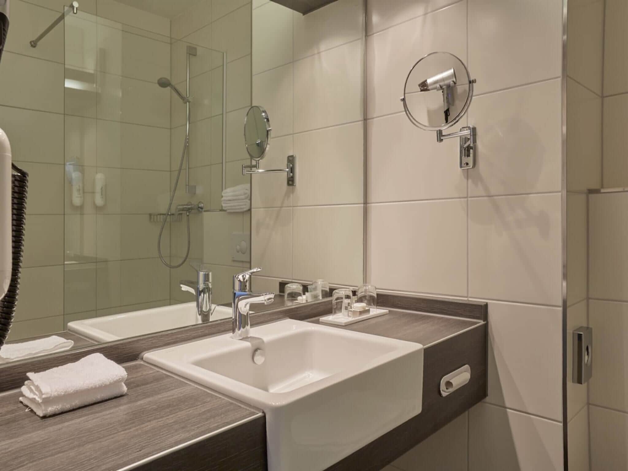 Uma casa de banho moderna com duas pias, chuveiro e secador de cabelo fixado na parede.