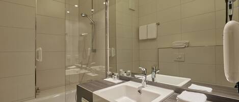 A modern bathroom with two sinks, a shower, and a large mirror.