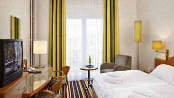 Een hotelkamer met een bed, een bureau met een televisie, een stoel, een klein tafeltje met een fles en een lamp.