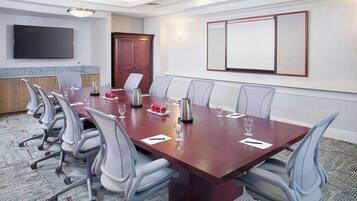 A conference room with a long table, chairs, a TV, and a large whiteboard.
