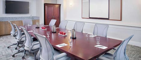 A conference room with a long table, chairs, a TV, and a large whiteboard.