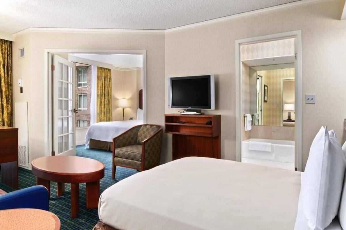 A hotel room with a bed, a television, a desk, a chair, a small table, and a bathroom.