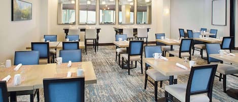 A hotel conference room with multiple tables and chairs, large mirrors on the walls, and a carpeted floor.