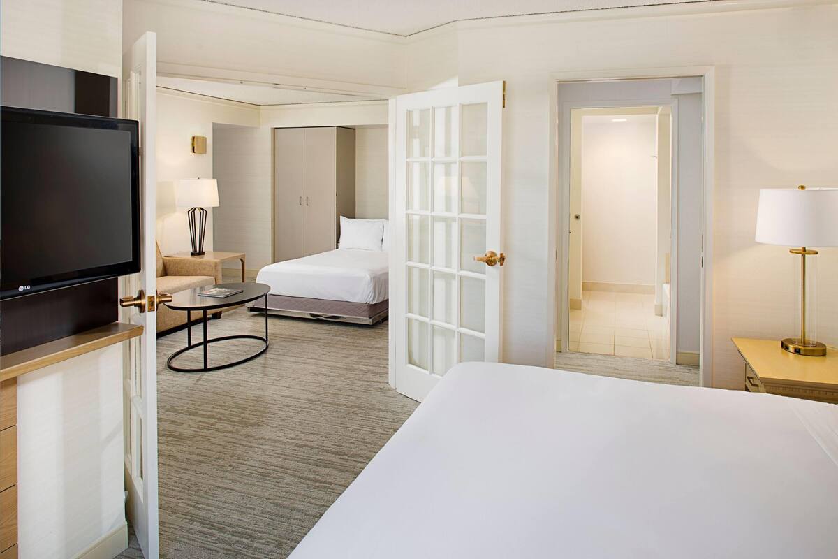 A hotel room with a bed, a TV, a desk, a chair, a lamp, and a wardrobe.
