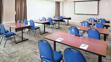 A conference room with multiple tables and chairs, equipped with water bottles and pens, and a projector screen on the wall.