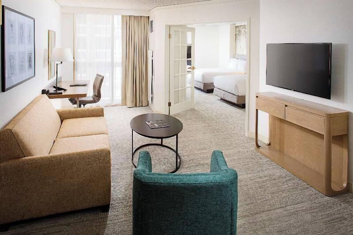 A hotel room with a sofa, a small round table, a TV, and a bed.