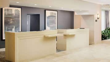 A reception area with two beige reception desks, a large window with a cityscape view, and a wall-mounted light fixture.