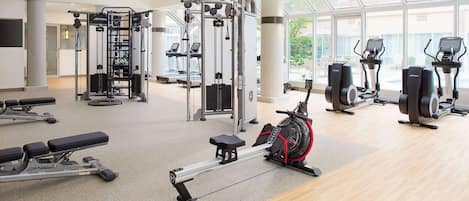 Un gimnasio con máquinas de cardio, equipo de entrenamiento con pesas y una máquina de remo.