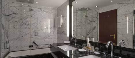 Een moderne badkamer met een grote spiegel, twee wasbakken, een douche en marmeren wanden.